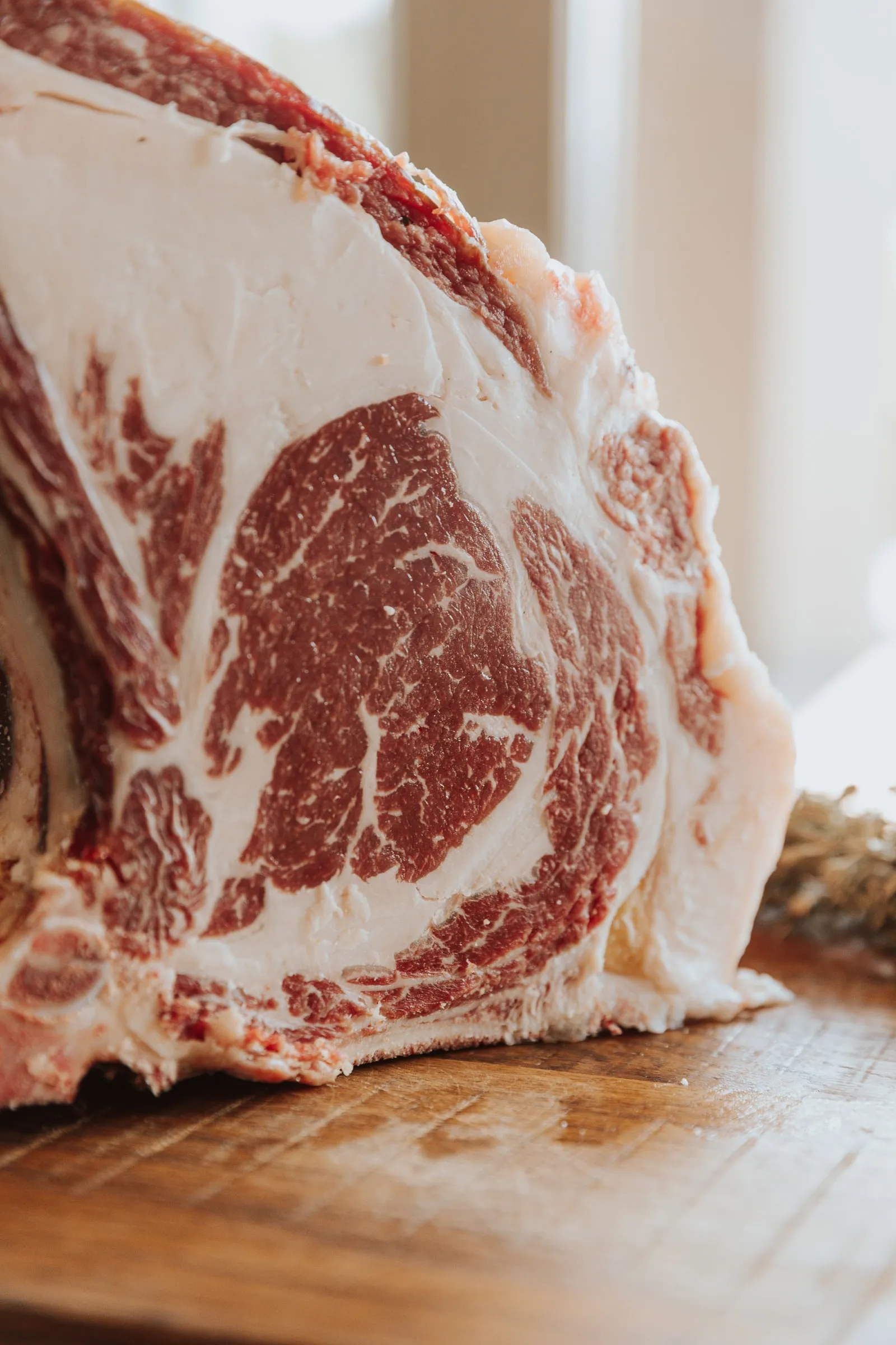 De snede van een rauw ribstuk van Angus Grand Cru, rechtop op een houten plank: fijne witte vetadertjes door het rode vlees, met een dikke vetrand eromheen