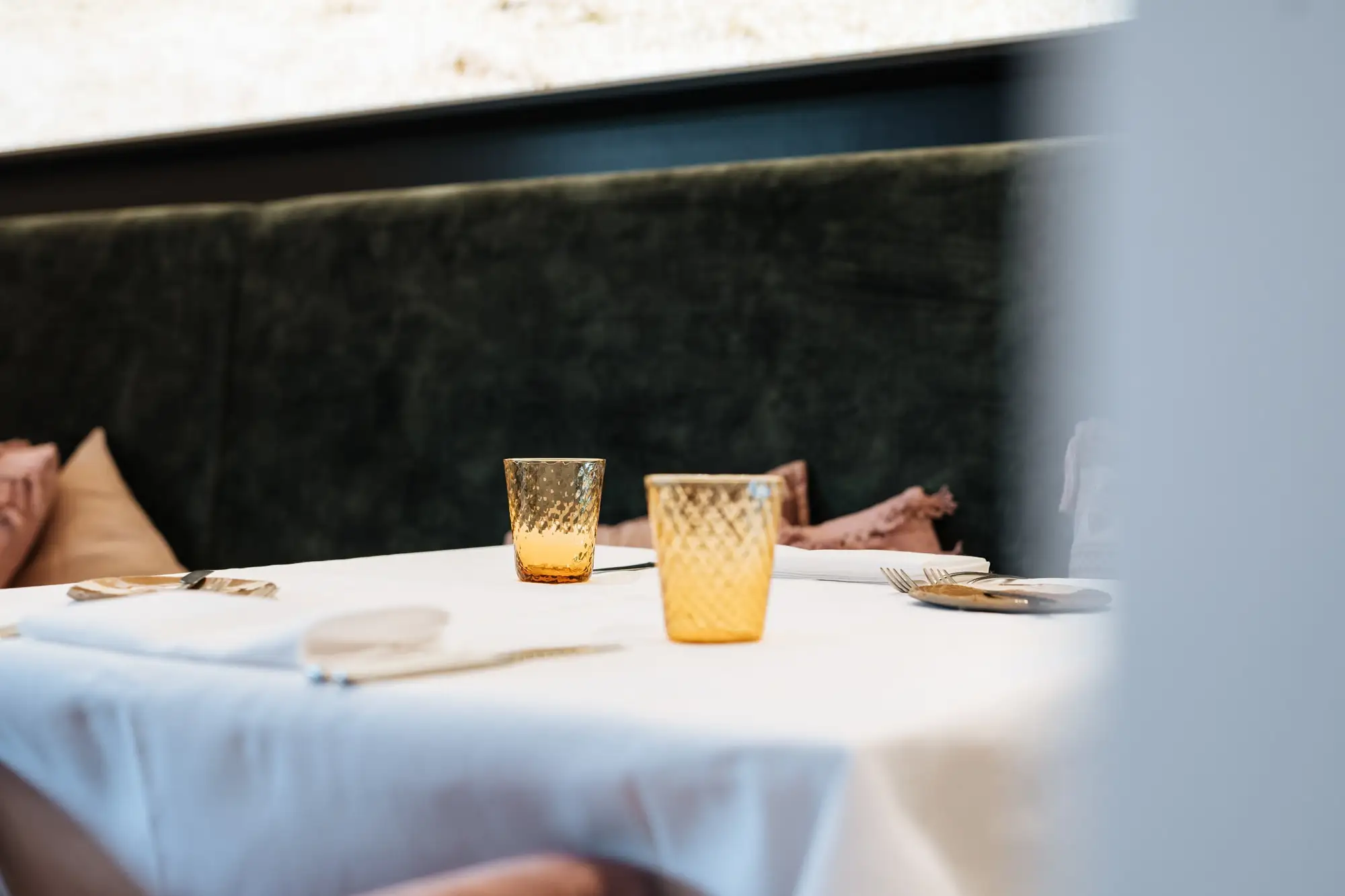 Amberkleurige glazen op een tafel met wit linnen, voor een donkergroene bank