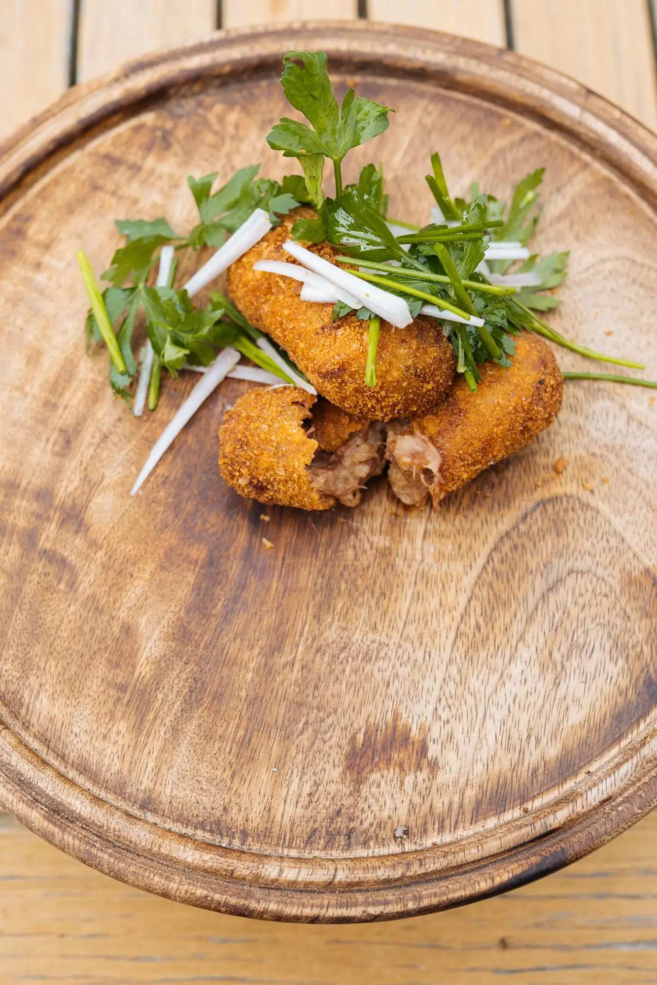 Kroketten met een toef kruiden op een houten bord